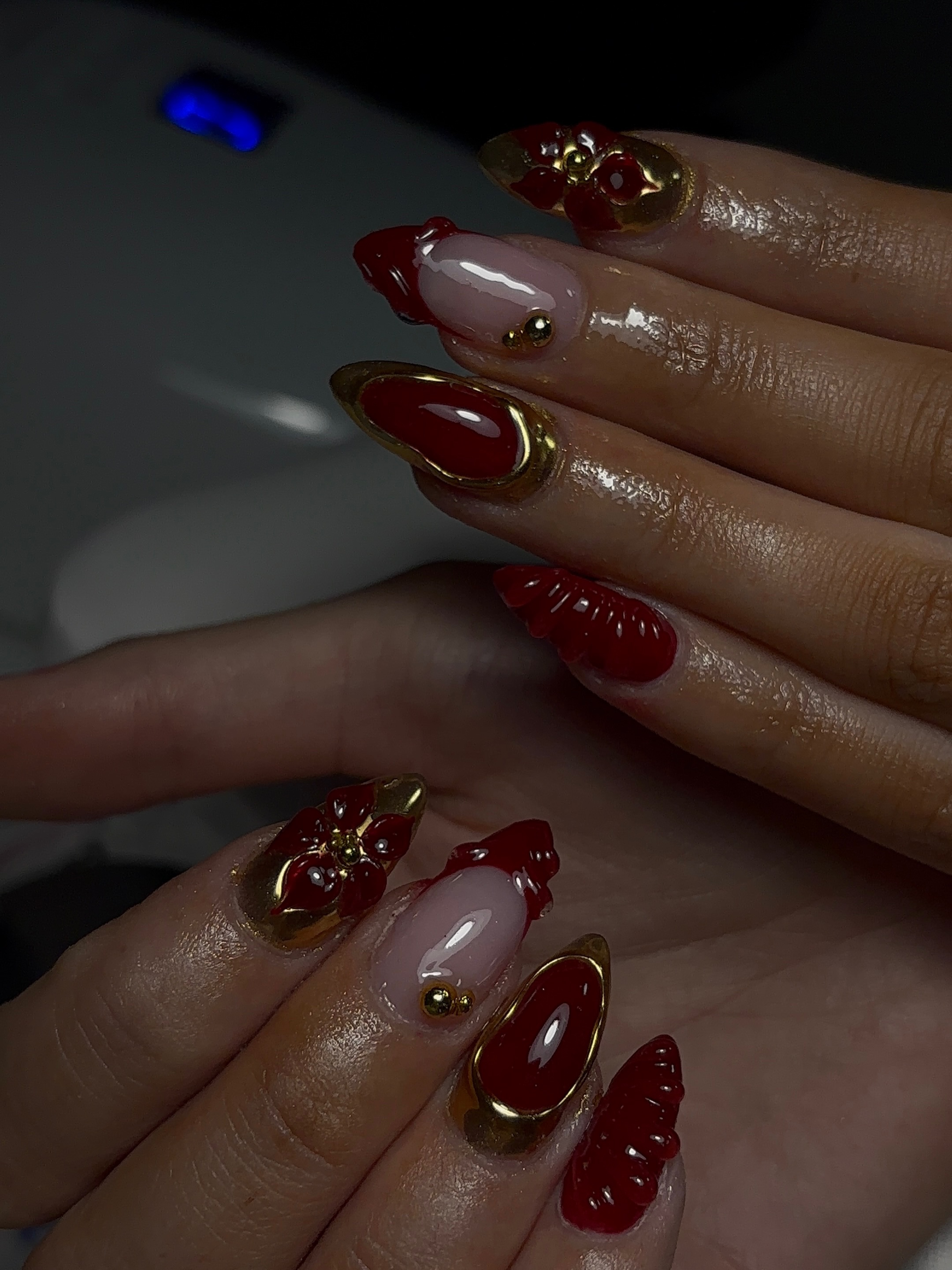 Donkerrode almond nagels met 3D bloemen en gouden rand